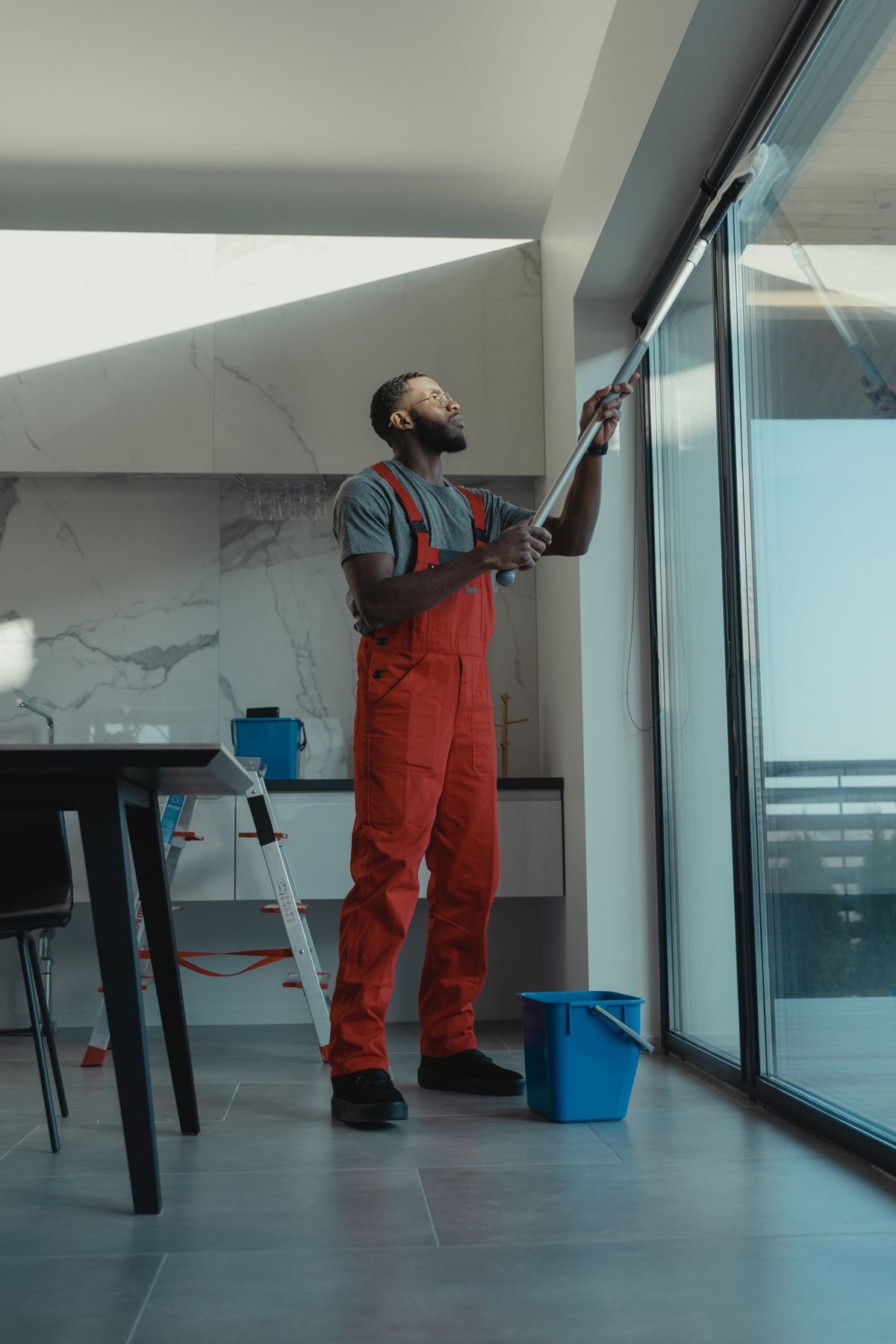 Professional cleaner wiping down a bright glass surface with a yellow-gloved hand