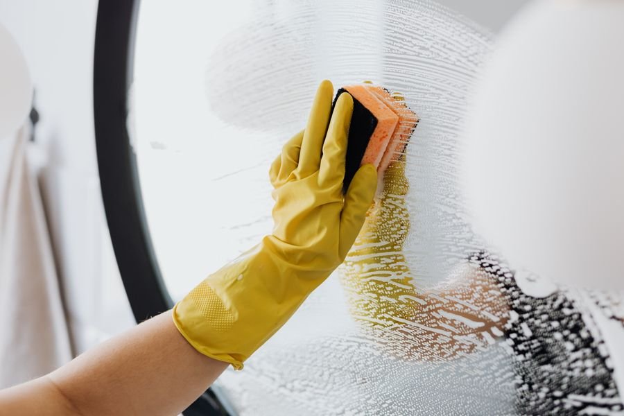 Cleaner in a yellow glove wiping a glass surface